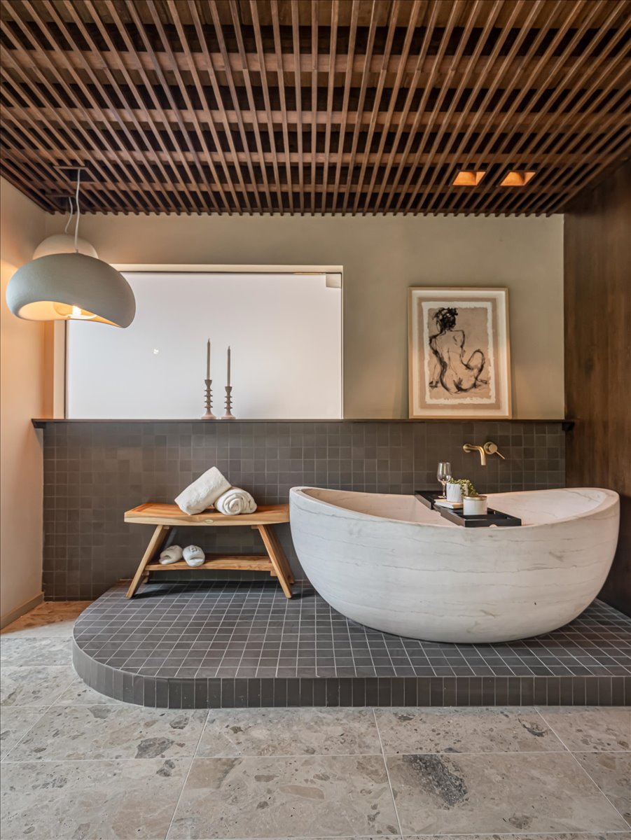 Freestanding soaking tub set on a raised platform with dark square tile