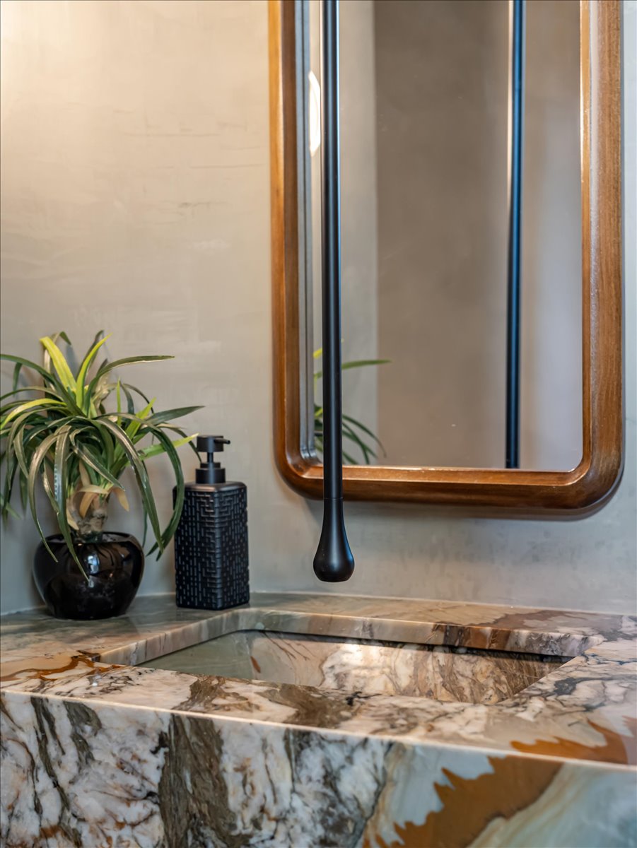 Integrated marble countertop and sink basin with natural patterning, a wall-mounted matte black faucet, and a mirror with a frame