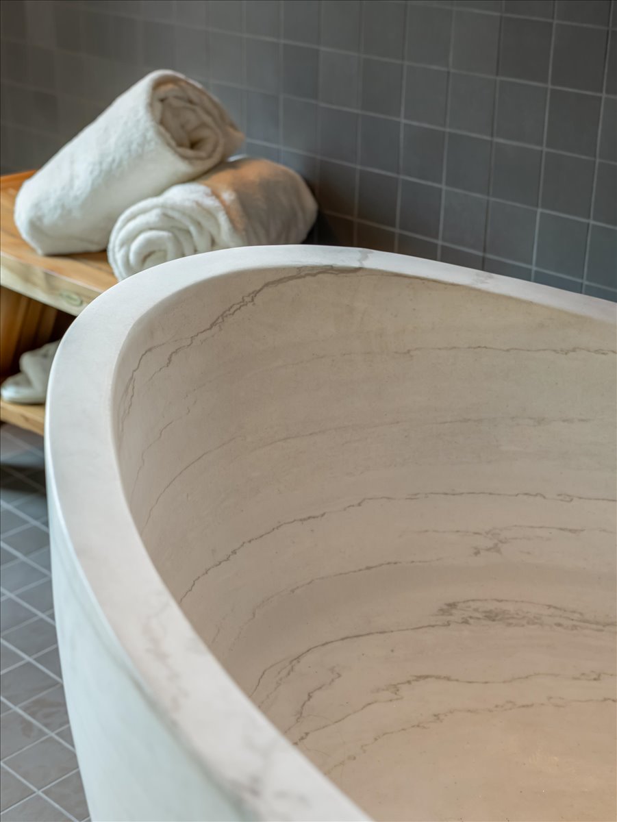 Freestanding soaking tub with a natural stone-look interior and a smooth, light-toned exterior