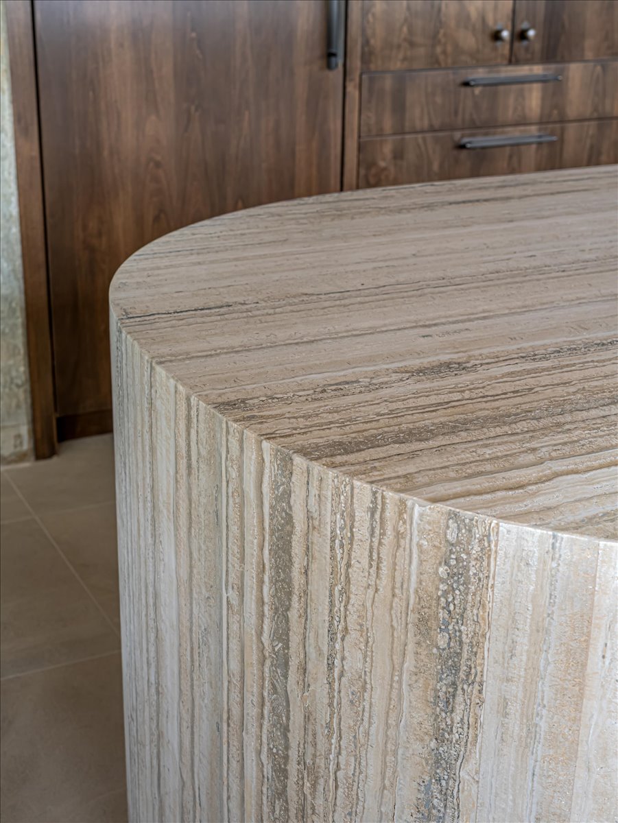 Curved stone island with natural striations, complemented by dark wood cabinetry featuring hardware and light-toned tile flooring