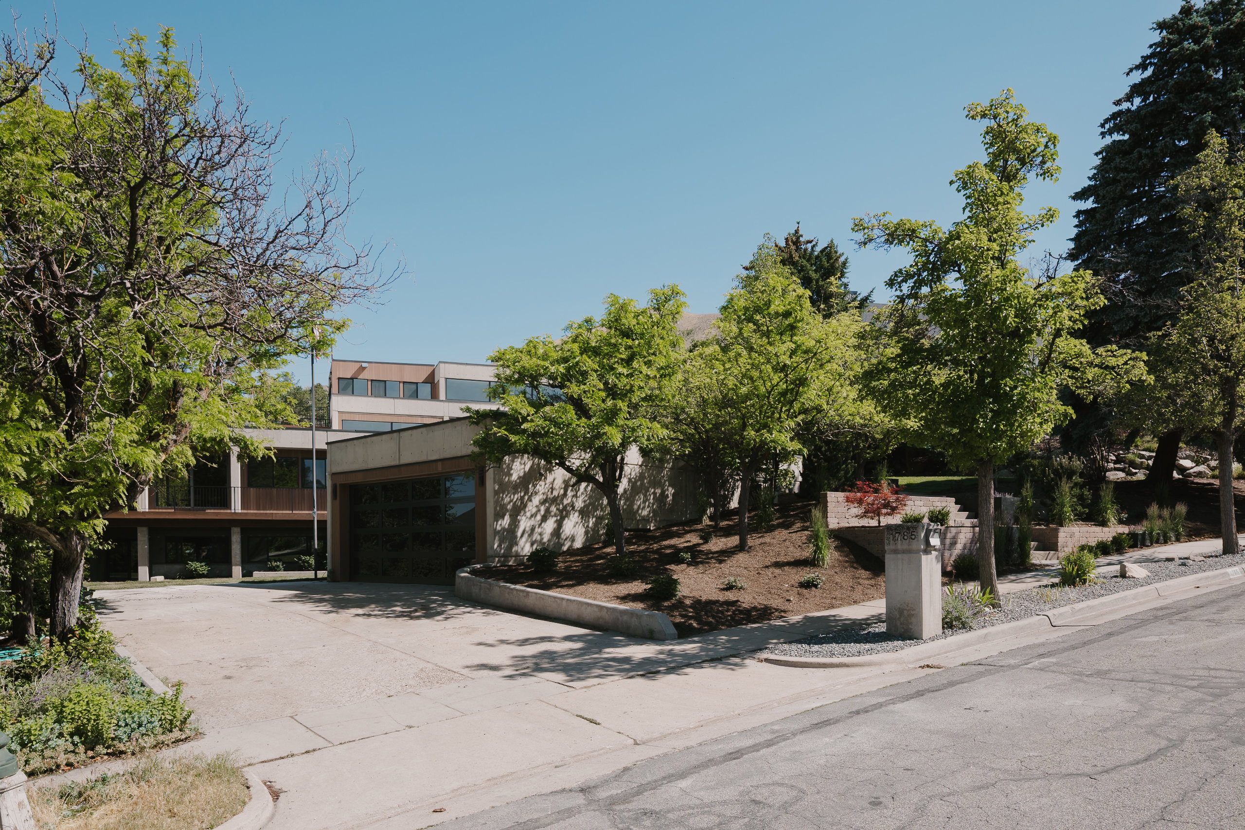 Contemporary multi-level residence featuring a concrete and wood-paneled exterior, integrated garage, and a long concrete driveway