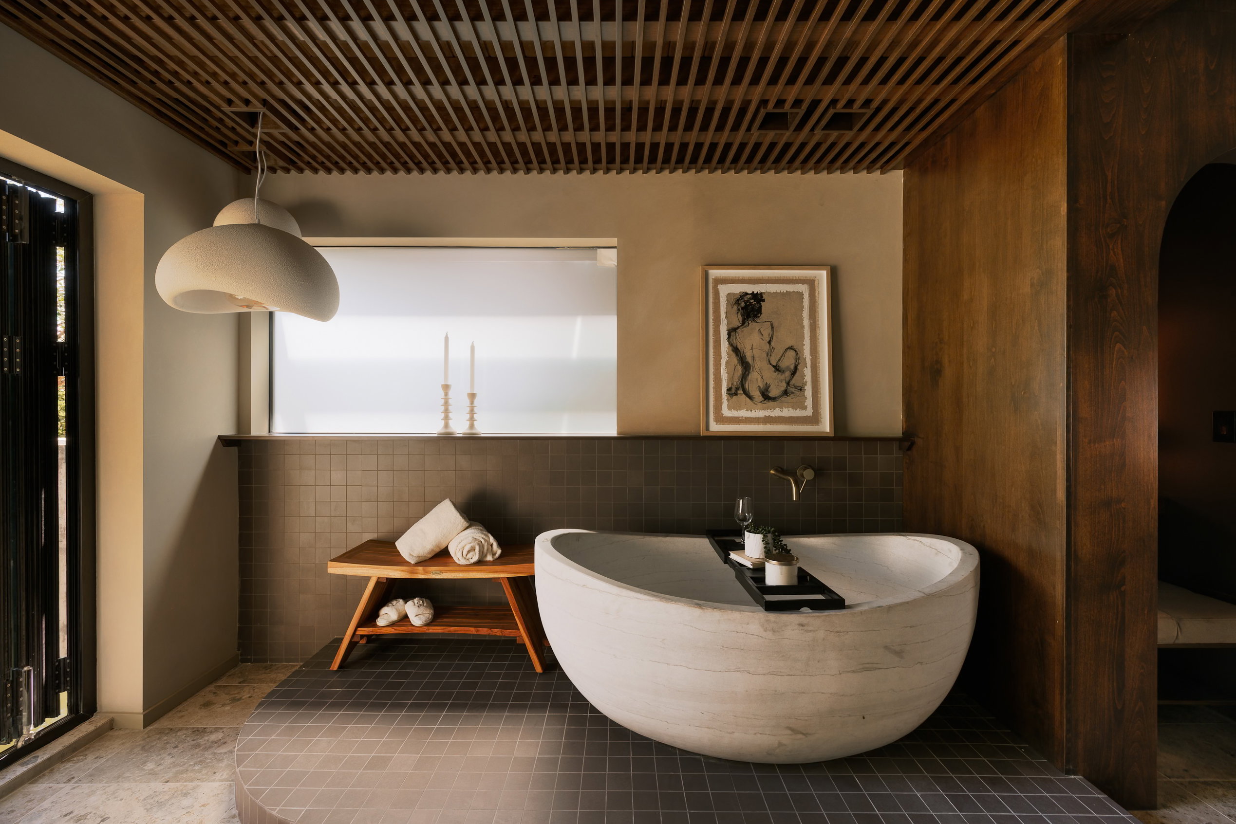 Luxurious bathroom featuring a freestanding soaking tub, wood-slat ceiling, dark tile flooring, and floor-to-ceiling accordion doors