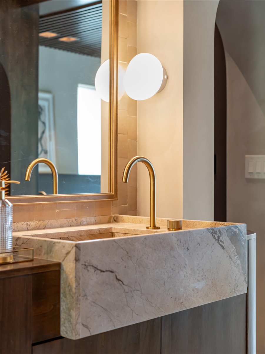 Stone vessel sink with integrated countertop, featuring a gold-finish faucet and brass-framed mirror