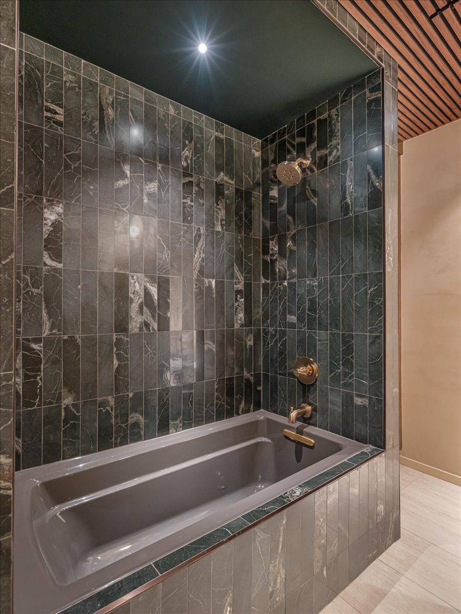 Built-in bathtub, brass fixtures, and surrounding full-height tile in a vertical pattern