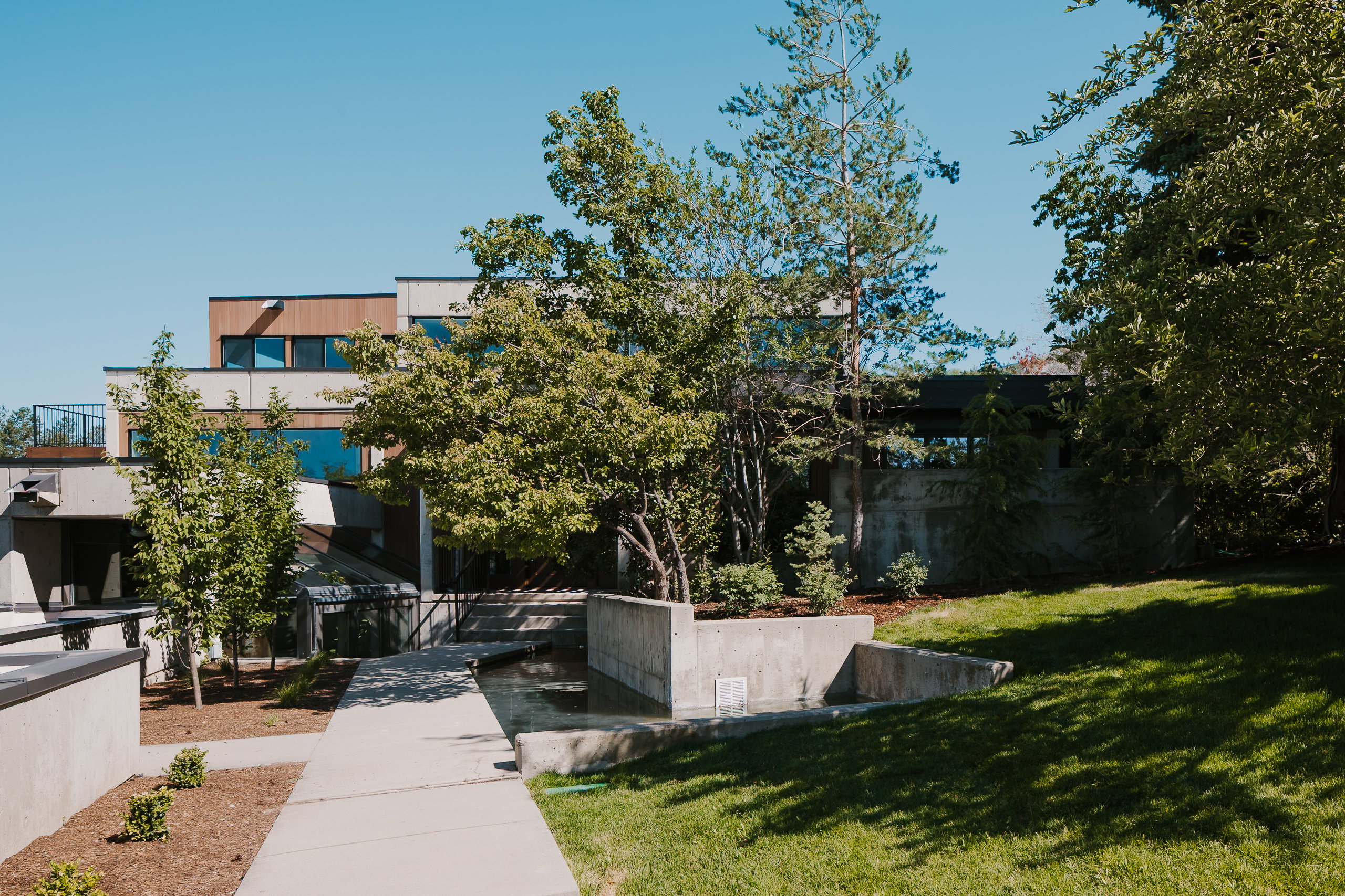 Modern multi-level exterior featuring varied cladding, extensive landscaping, concrete hardscaping, and a water feature