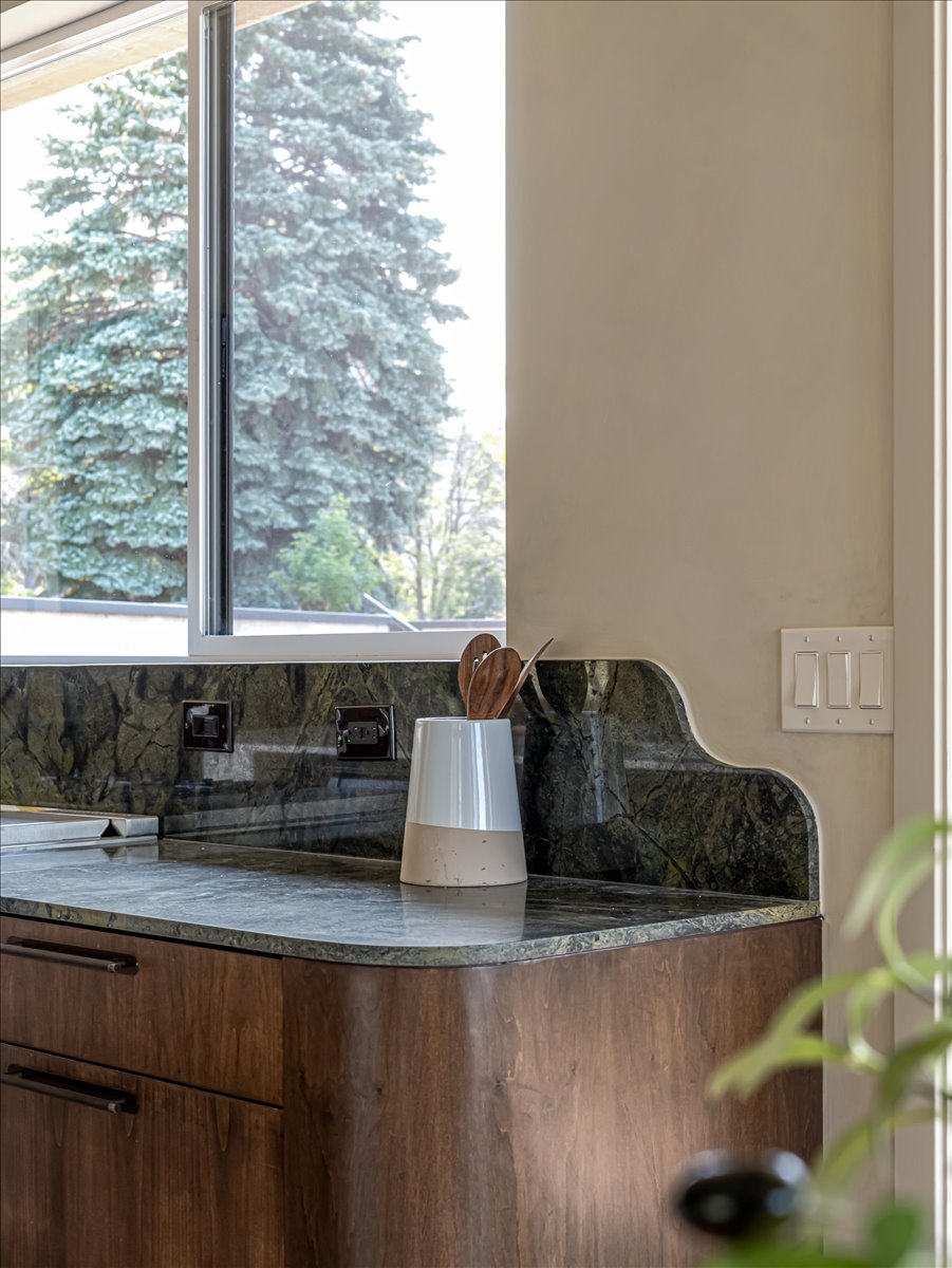 Curved wood-finish cabinetry with dark hardware, dark patterned stone countertops, and a matching stone backsplash