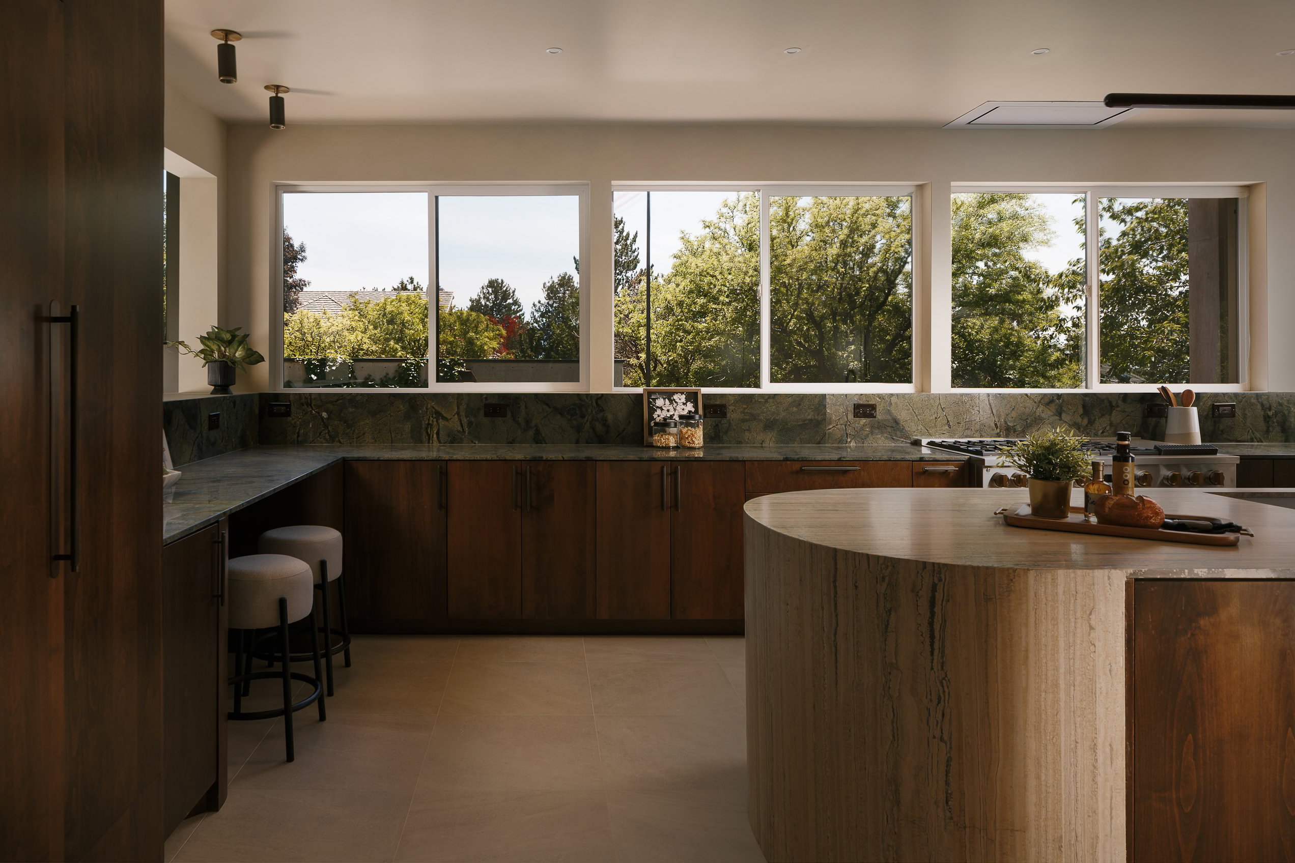 Gourmet kitchen featuring a curved center island, extensive green stone countertops, wood cabinetry, and multiple large windows