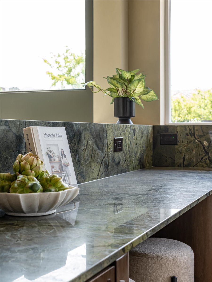 Polished stone countertop with matching backsplash, under-cabinet storage, and integrated electrical outlets