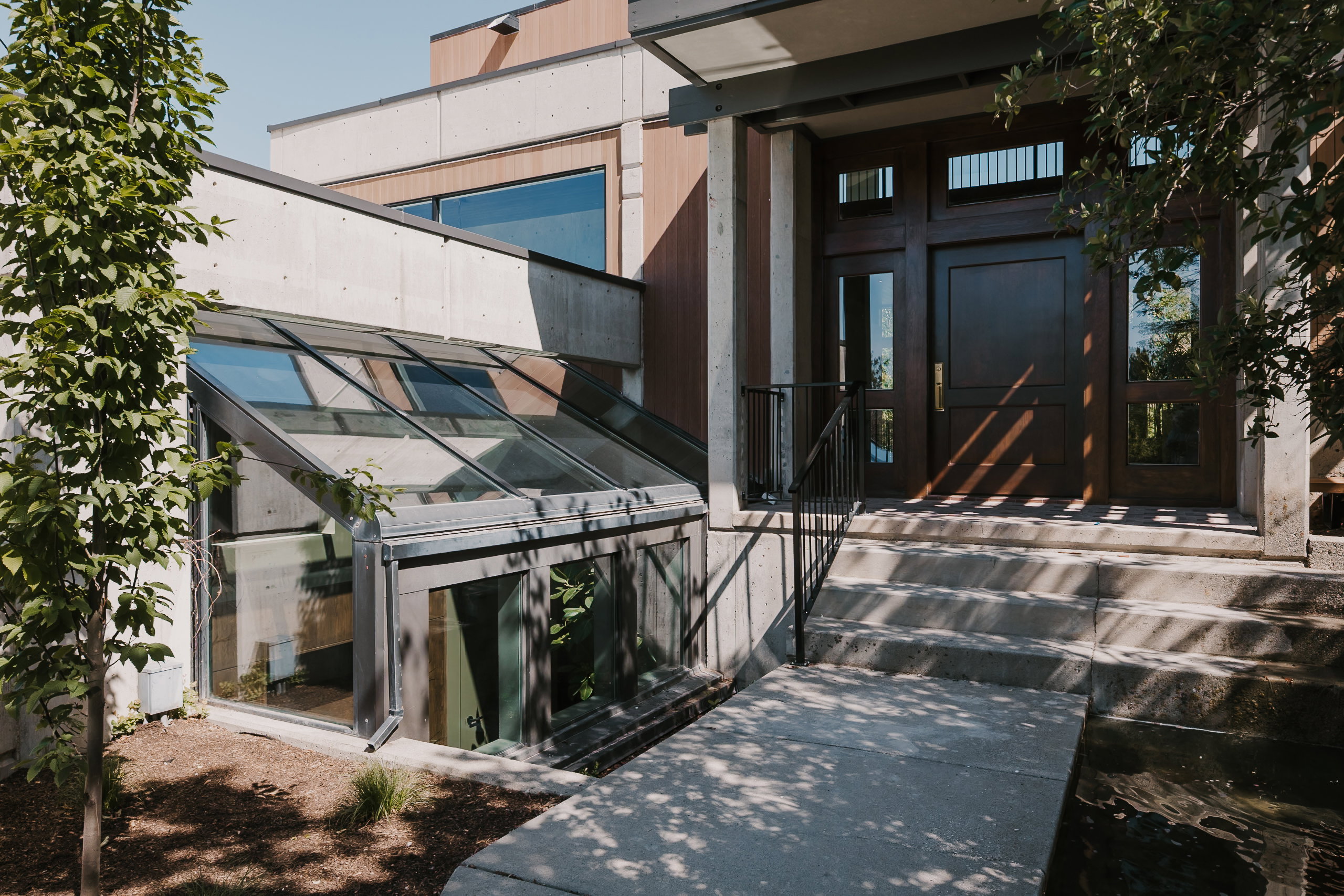 Modern concrete and wood-paneled exterior featuring a dark wood entry door with sidelights, a transom window, and a brass door handle