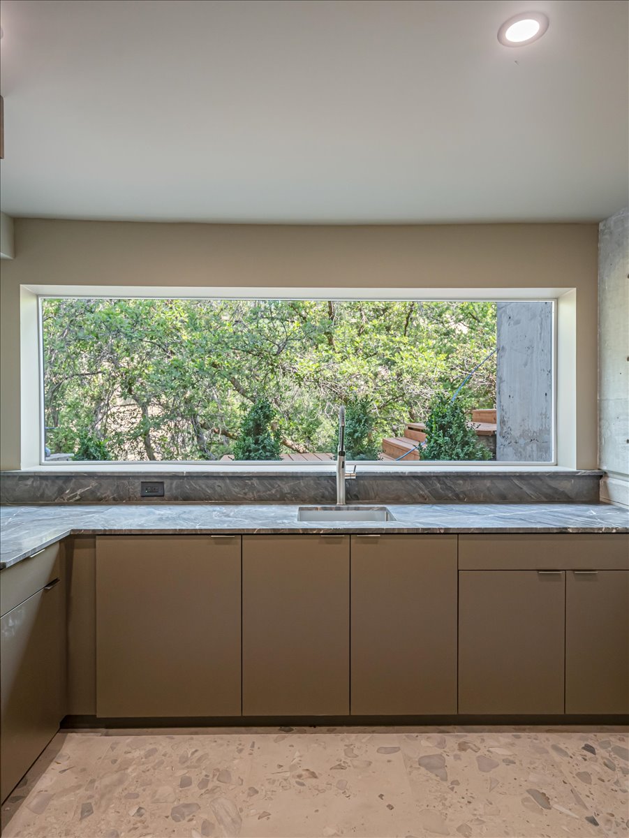 Kitchen featuring a wide horizontal window, dark gray countertop, under-mount sink with a stainless steel faucet, flat-panel cabinetry, and patterned flooring