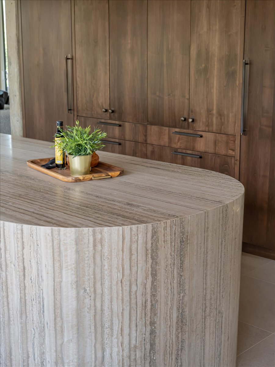 Curved stone island with vertical striations, complemented by tall wood cabinetry featuring black hardware and integrated panel-ready appliances