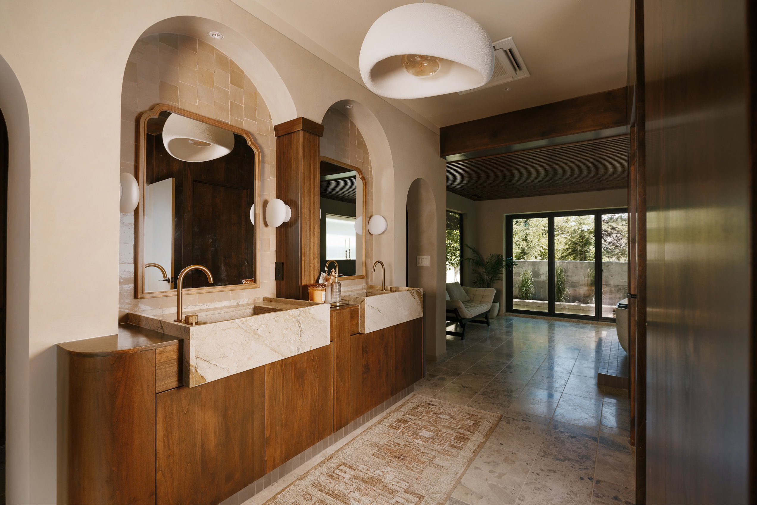 Double vanity featuring custom wood cabinetry, integrated stone sinks, and arched alcoves with decorative mirrors