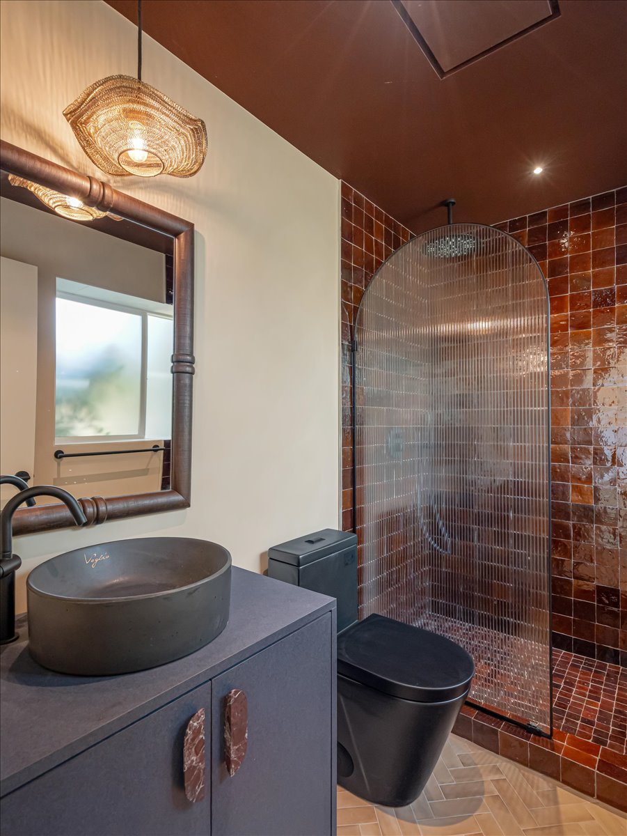Contemporary bathroom featuring an arched fluted glass shower enclosure, a vessel sink on a floating vanity, and a dark-toned toilet