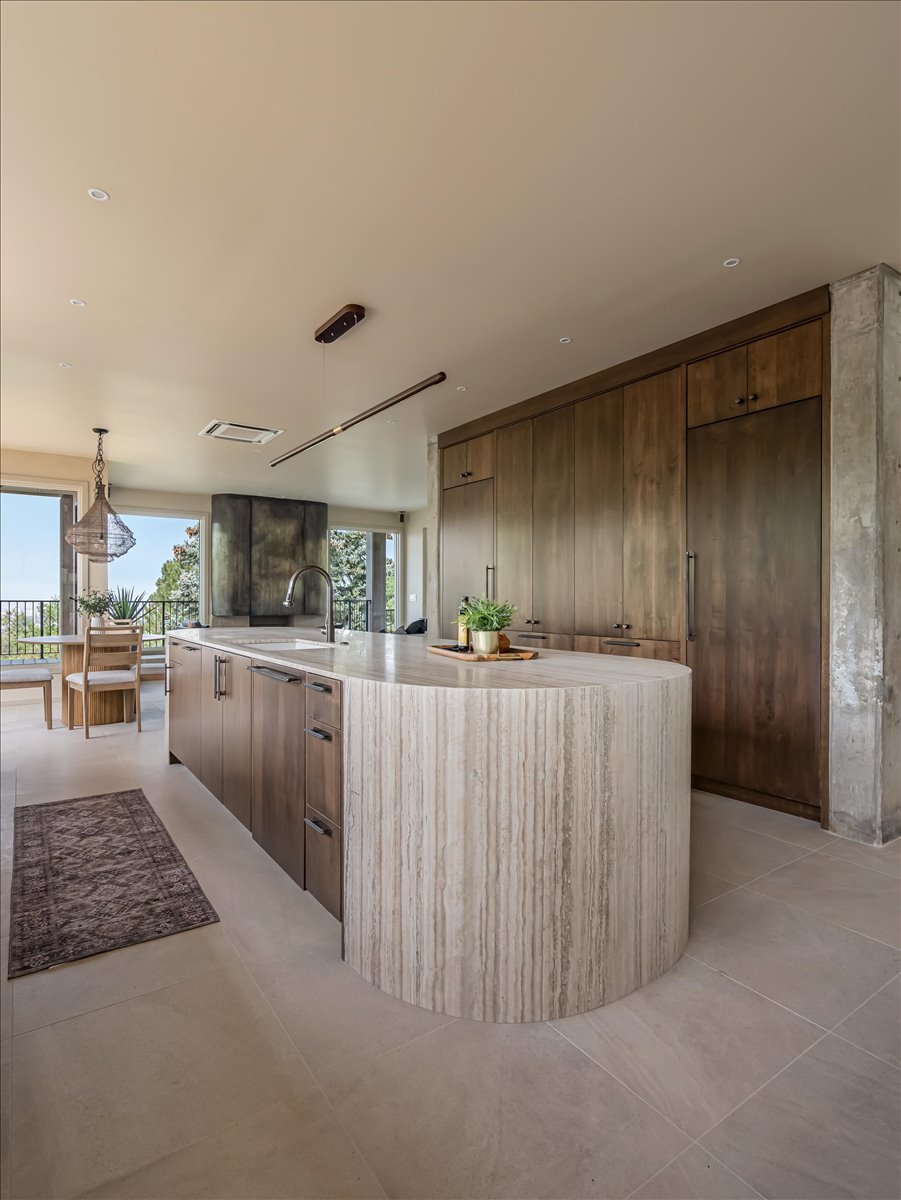 Gourmet kitchen with a rounded stone waterfall island, wood cabinetry, integrated appliances, and a contemporary linear pendant light