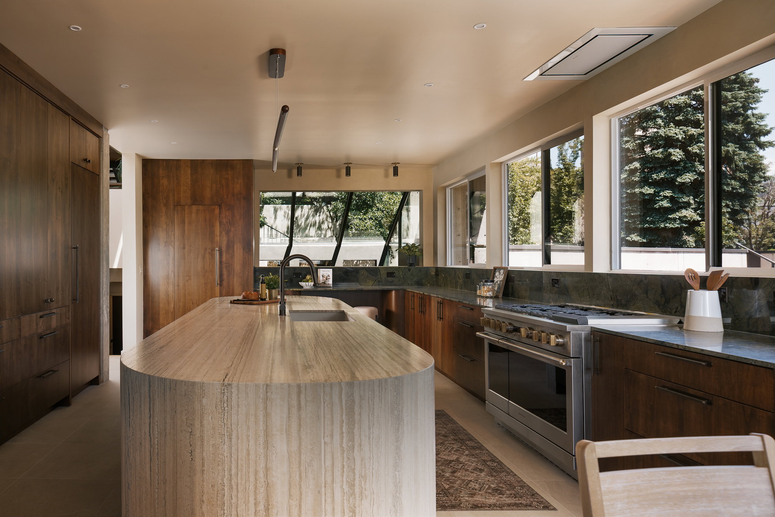Kitchen featuring a large curved island with an integrated sink, dark wood cabinetry, dark stone countertops, and stainless steel appliances
