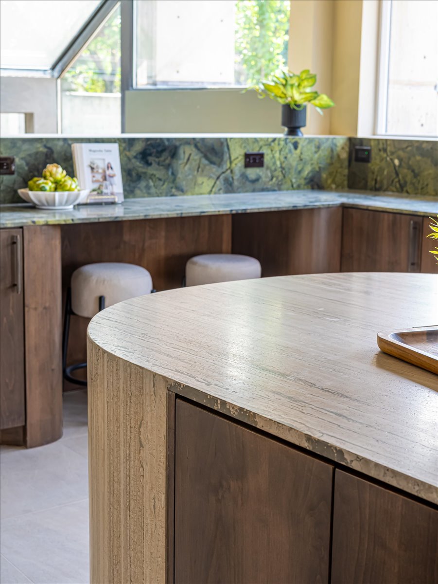 Kitchen featuring a curved island with a stone finish, dark wood-finish cabinetry, and green veined stone countertops and backsplash