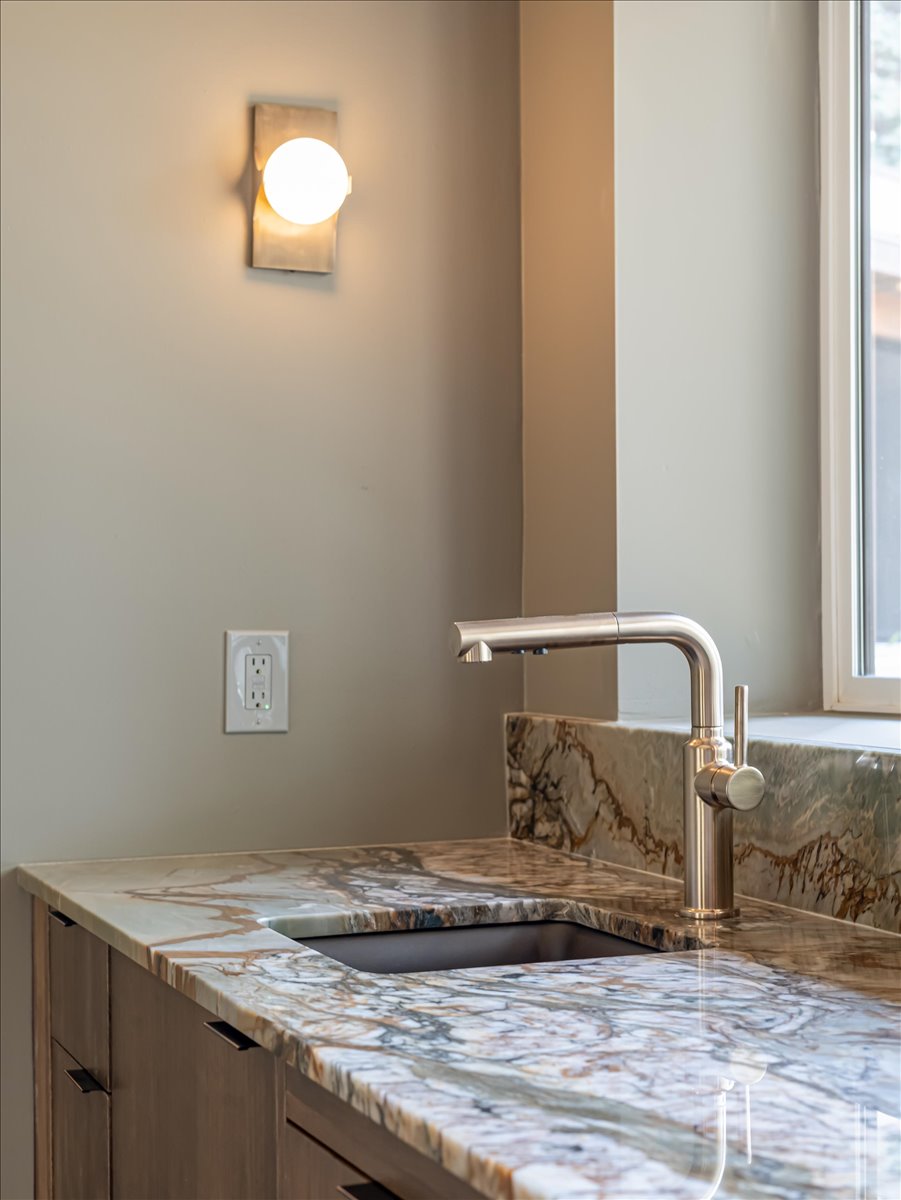 Featuring a polished stone countertop and backsplash, undermount sink, brushed nickel faucet, and integrated cabinetry
