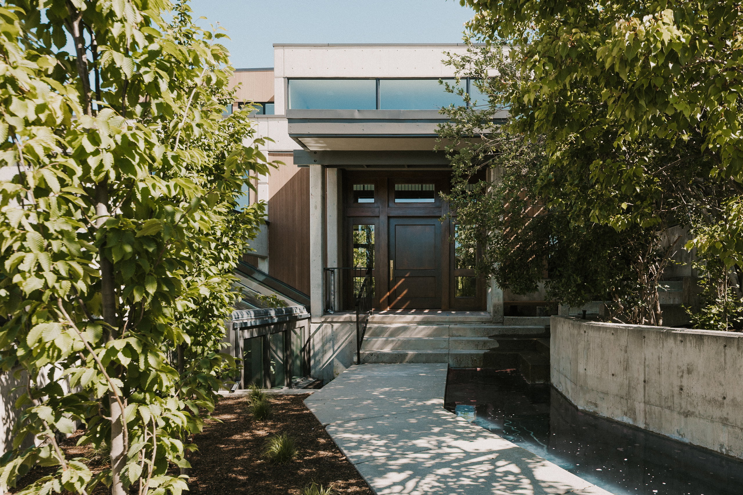 Modern architectural facade featuring a dark wood double entry door, concrete retaining wall, and a water feature