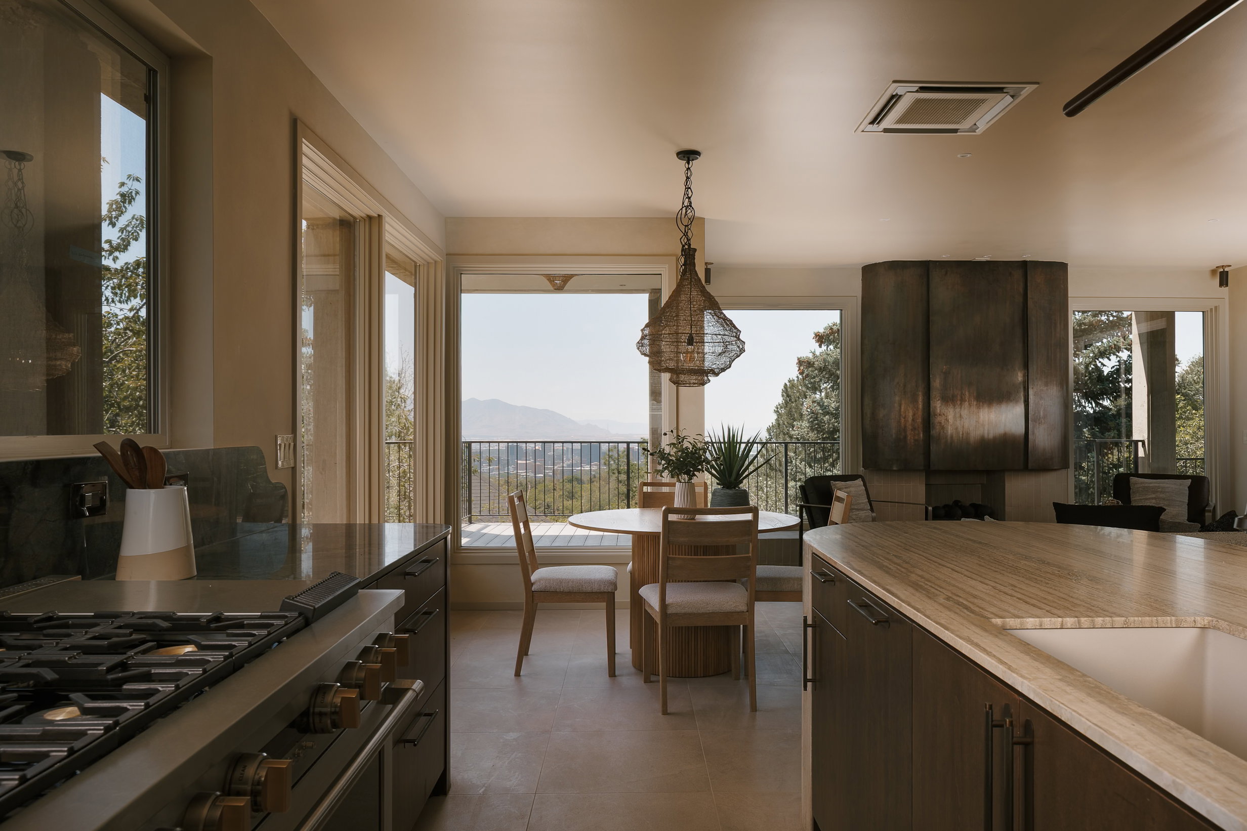 Open concept living space featuring a chef's kitchen with professional-grade range and stone countertops, dining area with a woven pendant light, and a prominent metal-clad fireplace