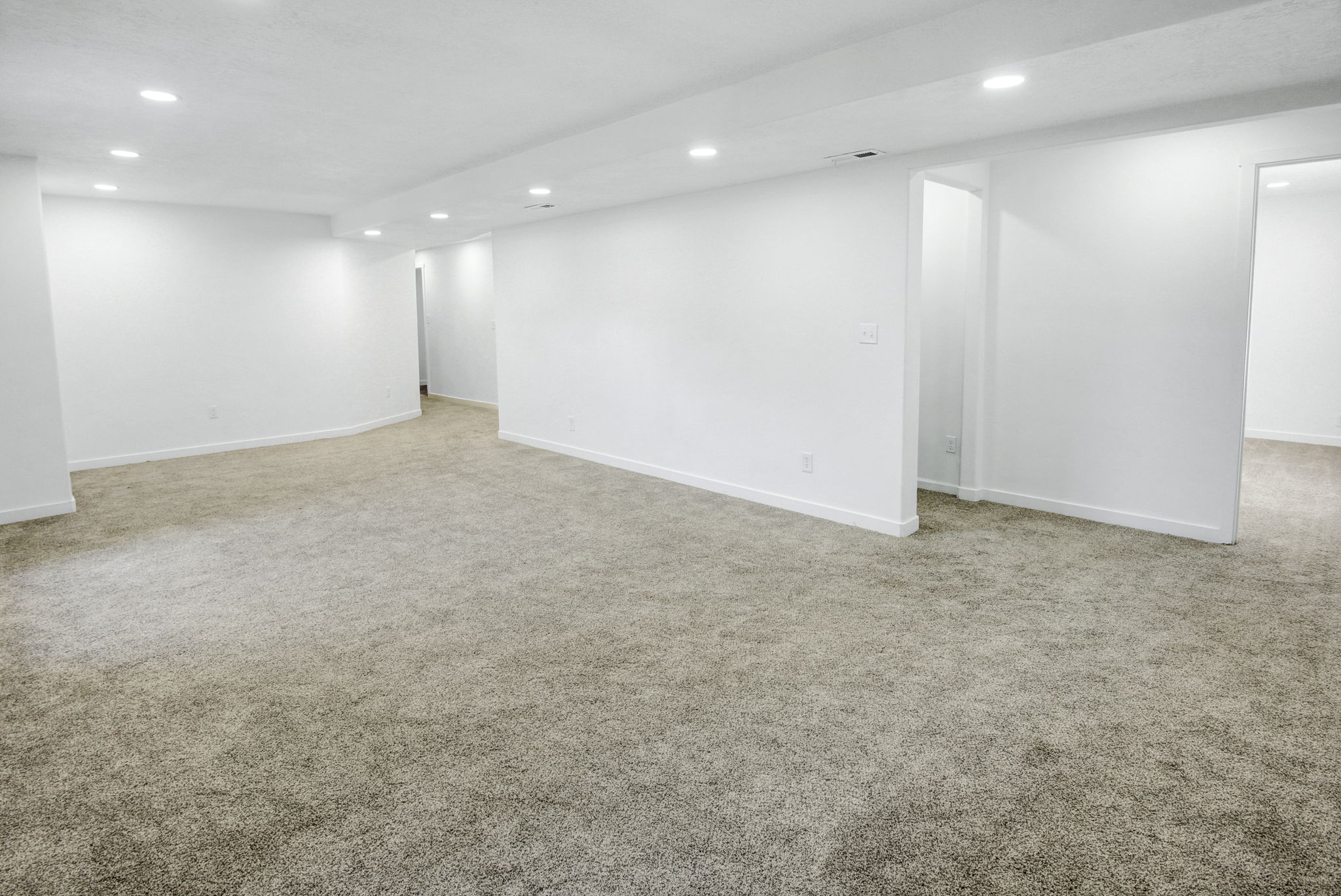 Spacious carpeted room featuring recessed lighting, bright white walls, and multiple entryways