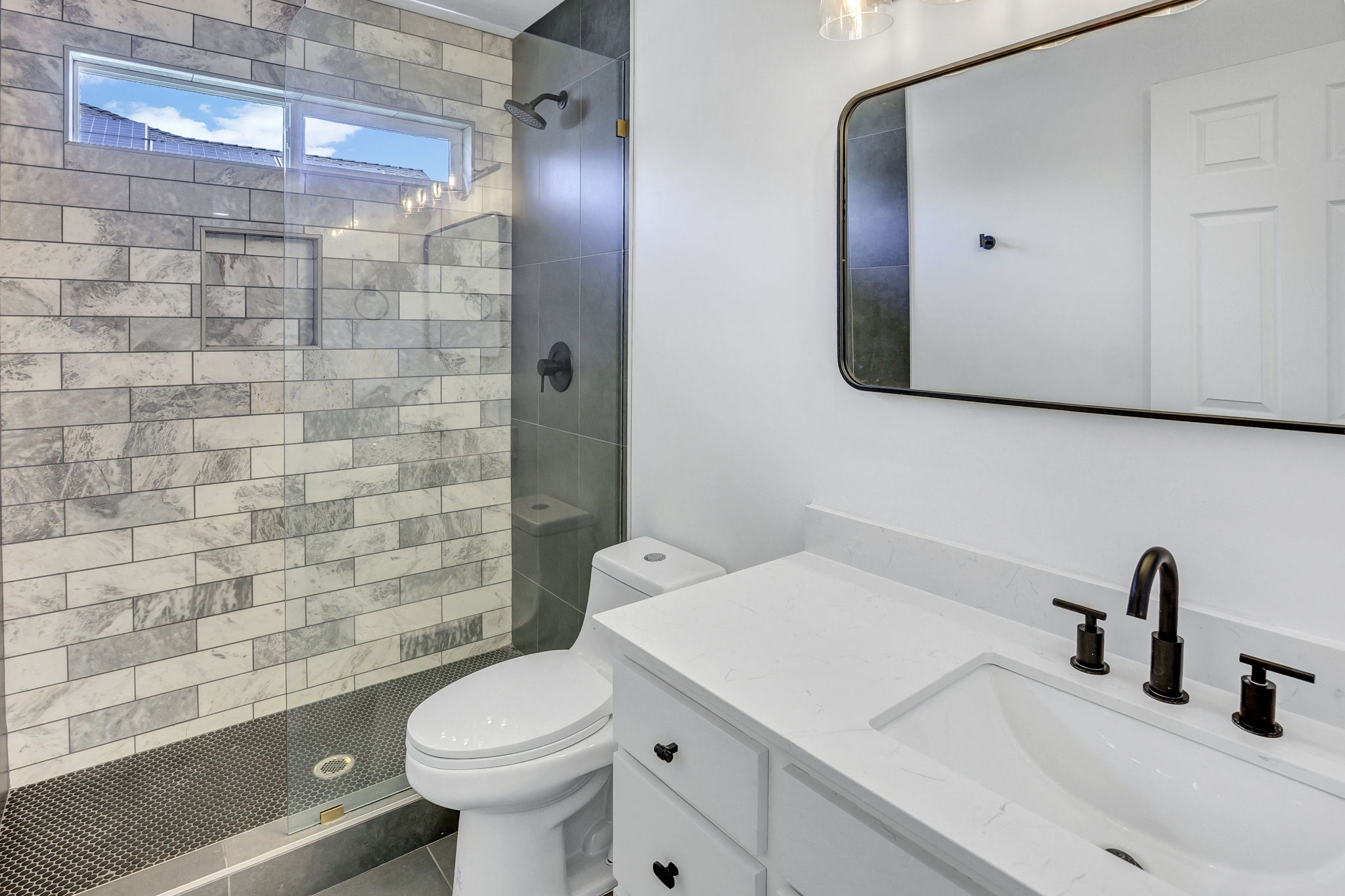Modern bathroom featuring a walk-in shower with subway tile surround, clear glass enclosure, and a transom window