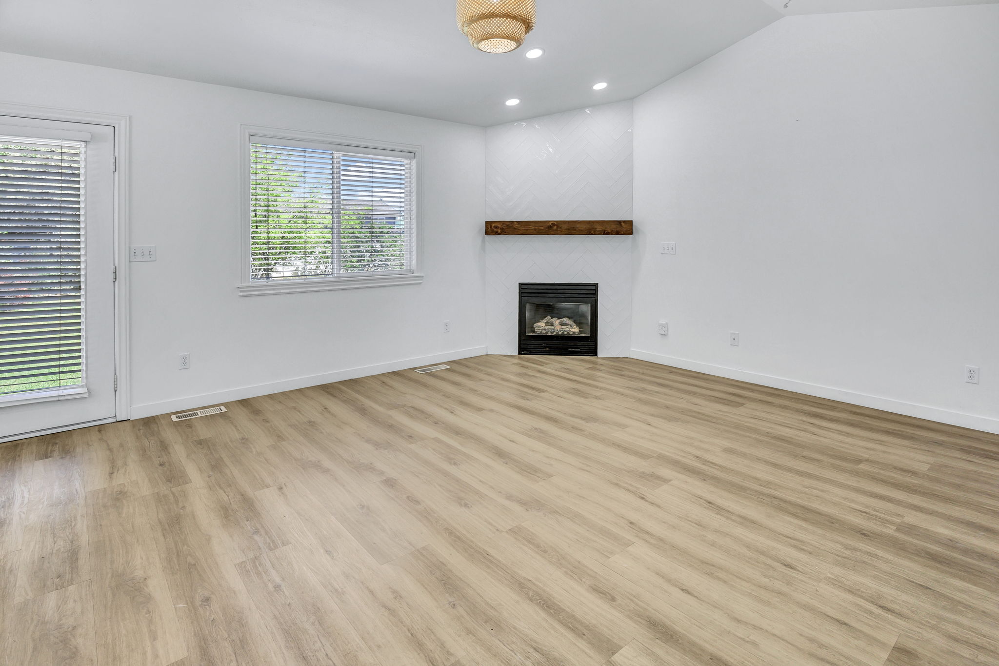Open-concept living space featuring wood-finish flooring, a contemporary fireplace with a wooden mantel, white chevron tile surround, and recessed lighting
