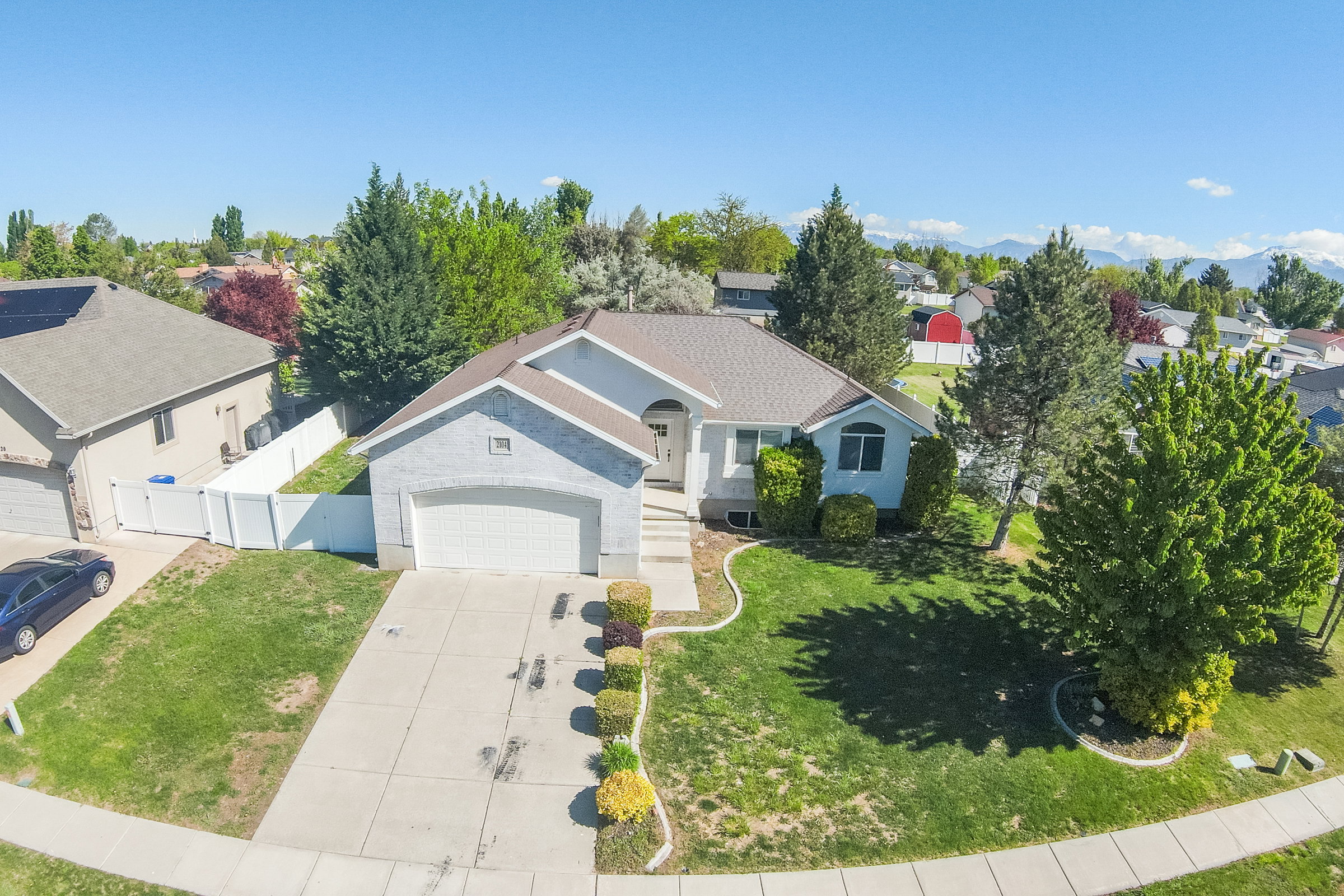 Single-story residence featuring a two-car garage, concrete driveway, and front lawn with mature trees and shrubbery