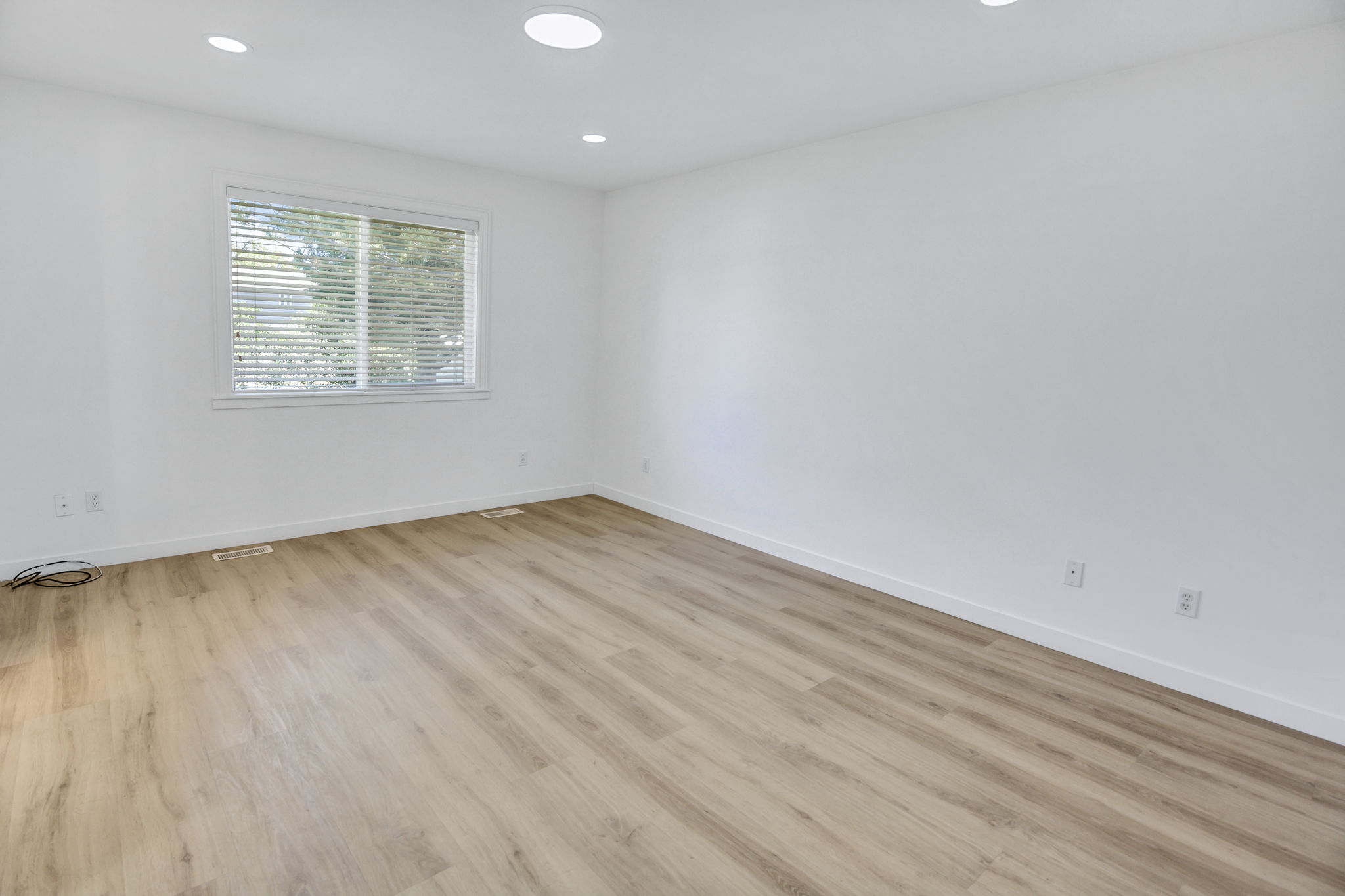 Spacious room featuring light wood-finish flooring, recessed lighting, and a window with blinds