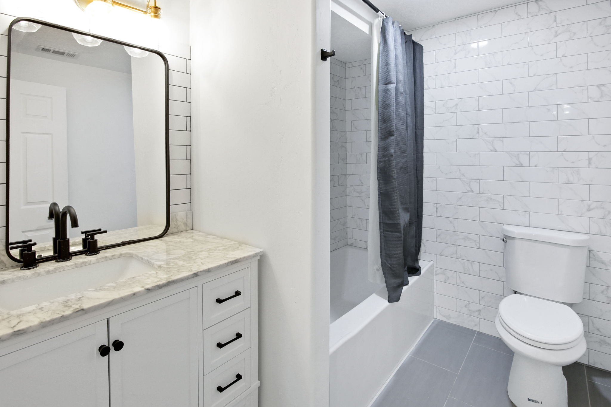 Bathroom with a white vanity featuring a light-toned countertop, black hardware, and a framed mirror