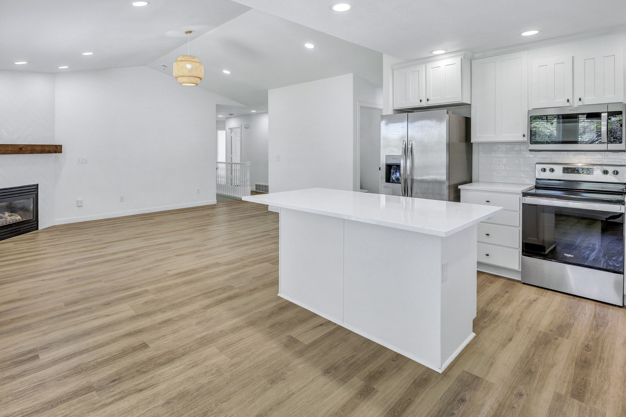 Open-concept living space with wood-finish flooring, a contemporary fireplace with a wood mantle, and recessed lighting