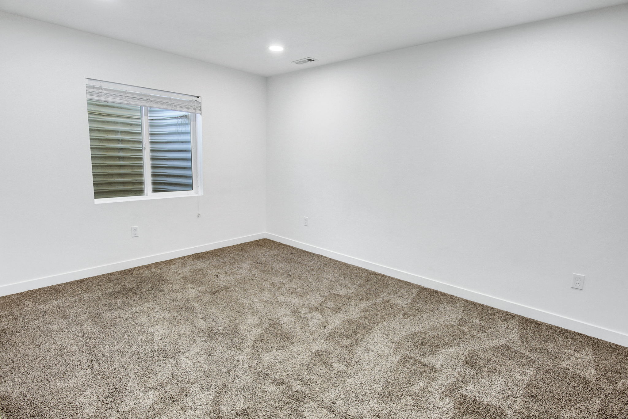 Bright room featuring a window with blinds, recessed lighting, and neutral-toned carpet