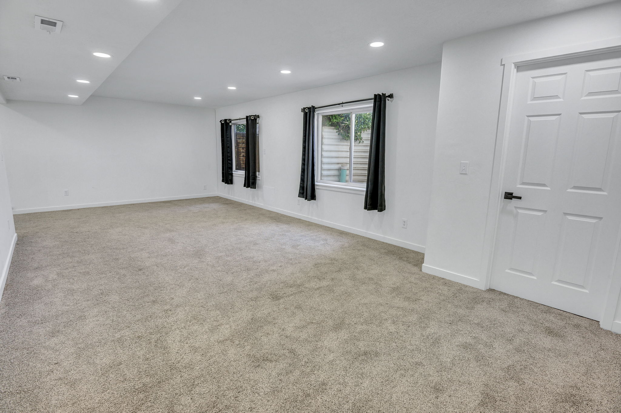 Spacious room featuring light-colored carpeting, white walls, and recessed lighting