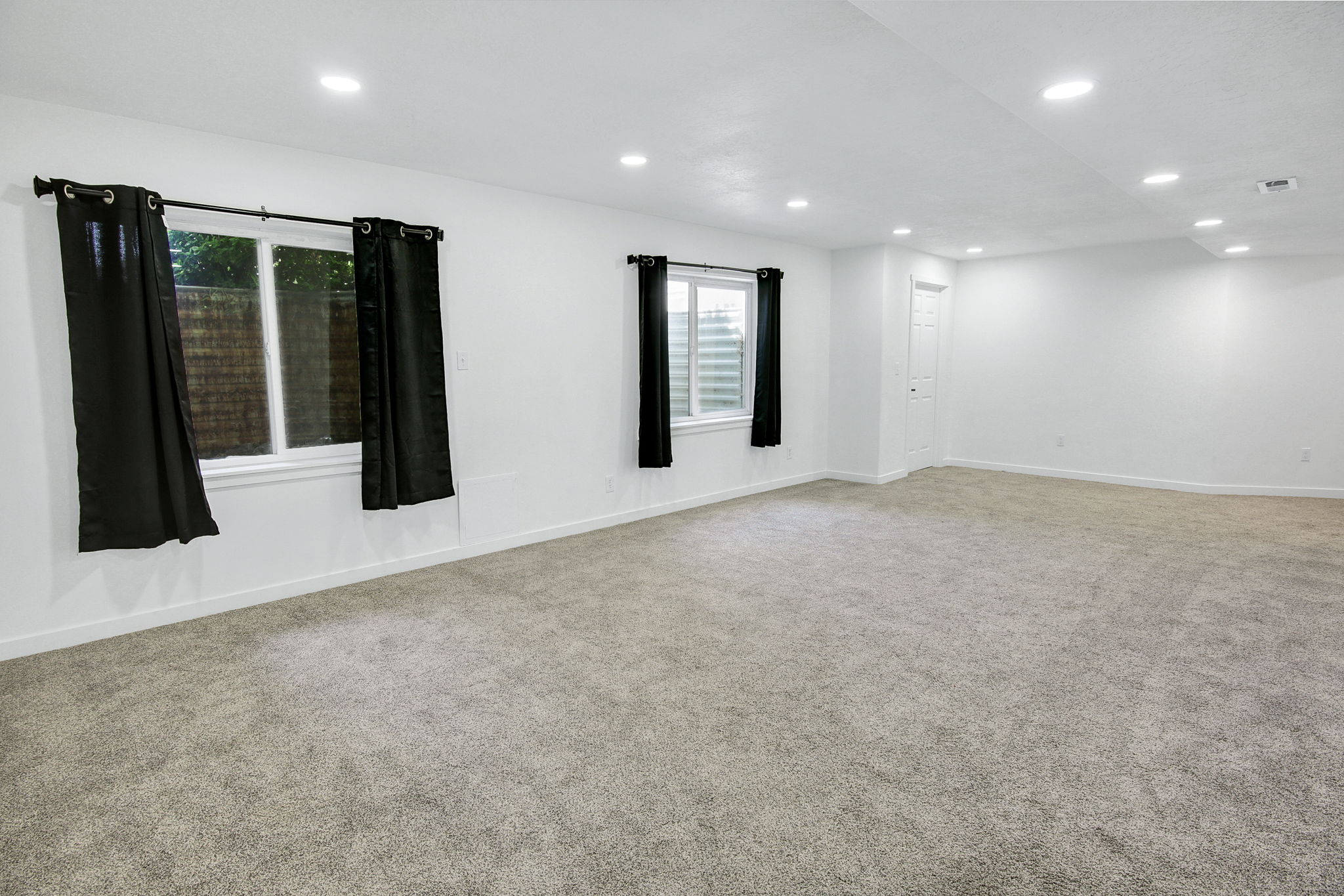 Spacious room featuring light-toned carpeting, white walls, and recessed lighting