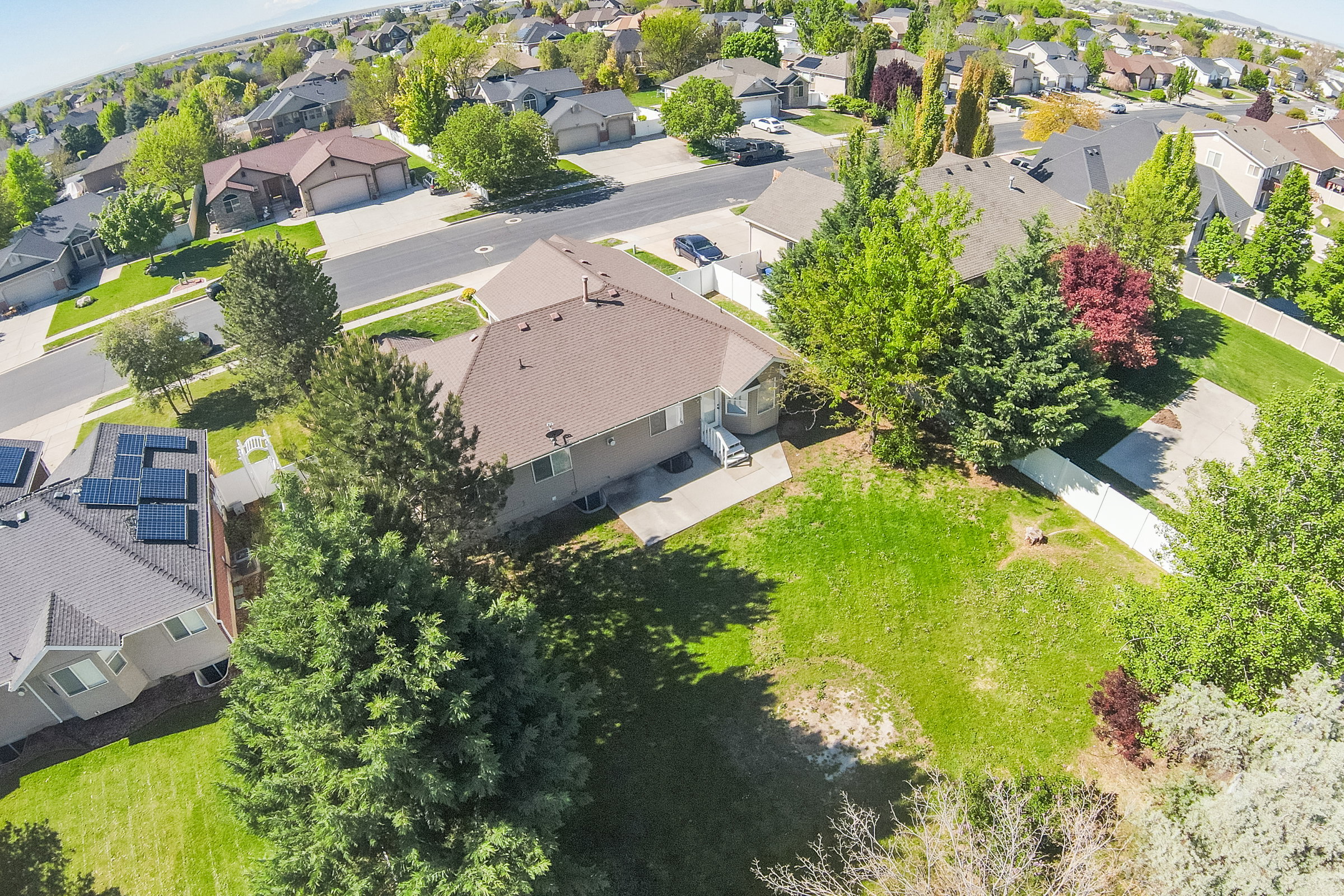Suburban property featuring a large backyard with mature trees, a concrete patio, and a sloped roof