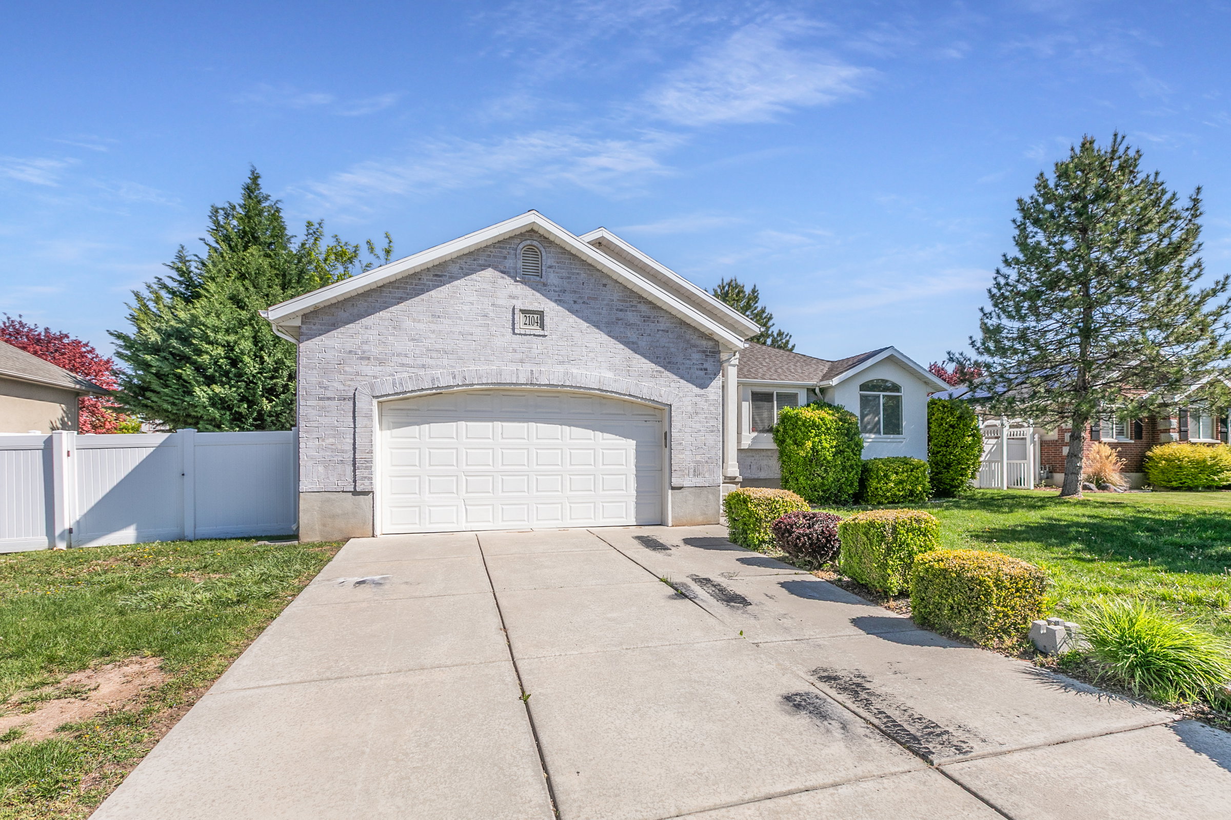 White brick exterior featuring a two-car garage with an arched opening, a concrete driveway, and established front landscaping