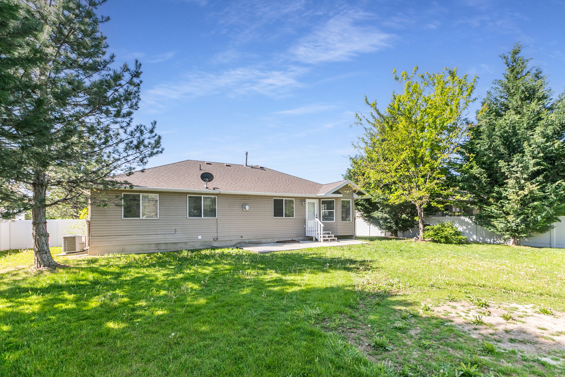 Expansive backyard featuring a lush lawn, mature trees, and a white privacy fence