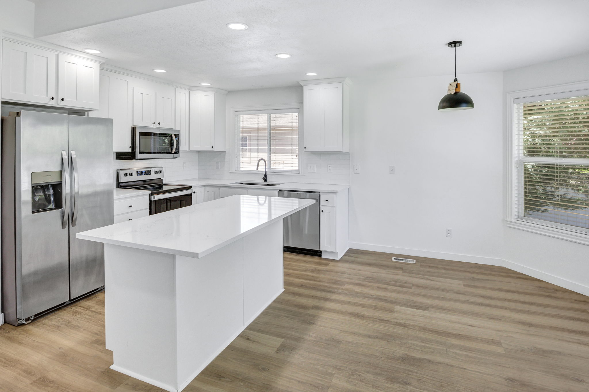 Modern kitchen featuring a central island with white countertop, white cabinetry, stainless steel appliances, and wood-finish flooring