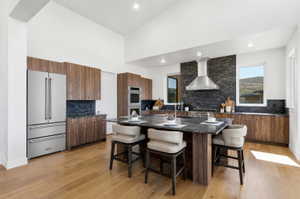 Open-concept kitchen featuring vaulted ceilings, wood-finish cabinetry, a large stone-topped island, stainless steel appliances, and wood-finish flooring