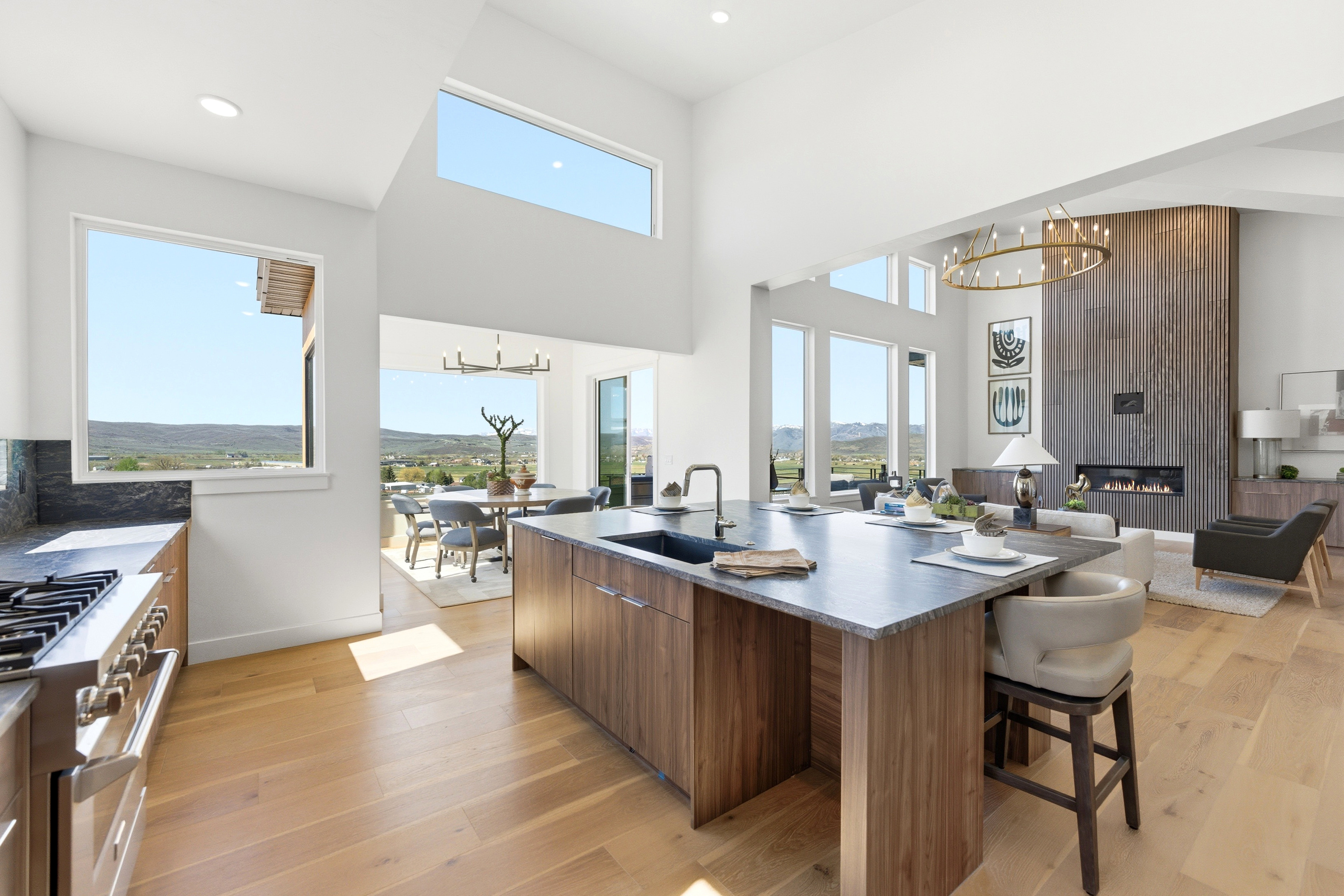 Open-concept living space featuring a spacious kitchen island with seating, a built-in range, wood-finish flooring, and a contemporary fireplace with a tall wood-paneled surround