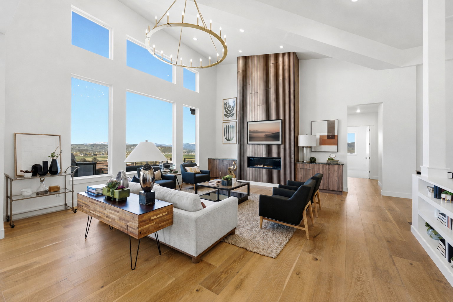 Spacious living area featuring expansive windows, wood-finish flooring, a vaulted ceiling, a linear fireplace with wood-paneled surround, and a large circular chandelier, TV virtually staged