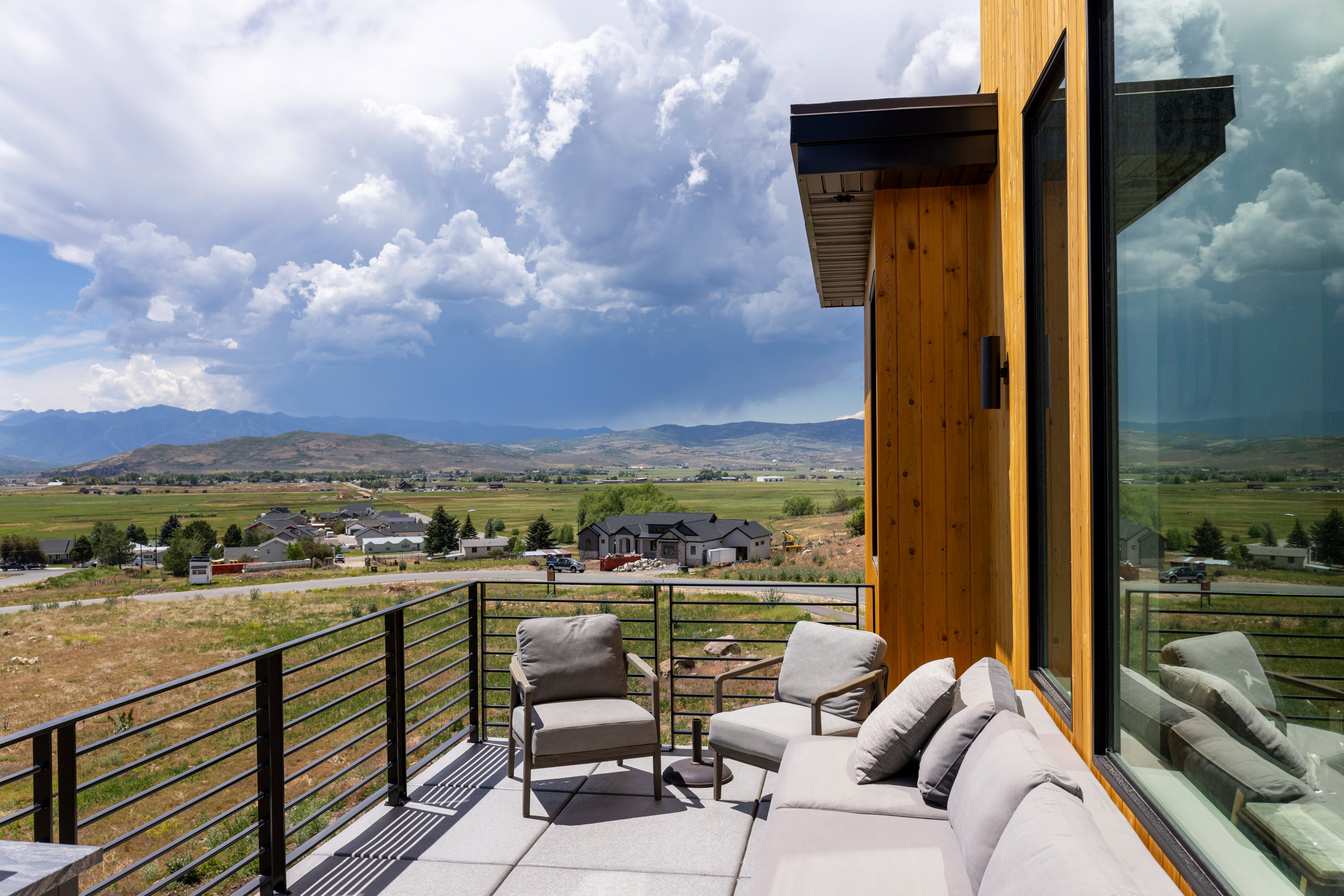 Exterior balcony featuring modern horizontal metal railings, concrete flooring, and a natural wood-finish wall panel