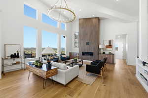 Spacious living area featuring expansive windows, wood-finish flooring, a contemporary linear fireplace set in a wood-paneled accent wall, a vaulted ceiling, and a large circular chandelier