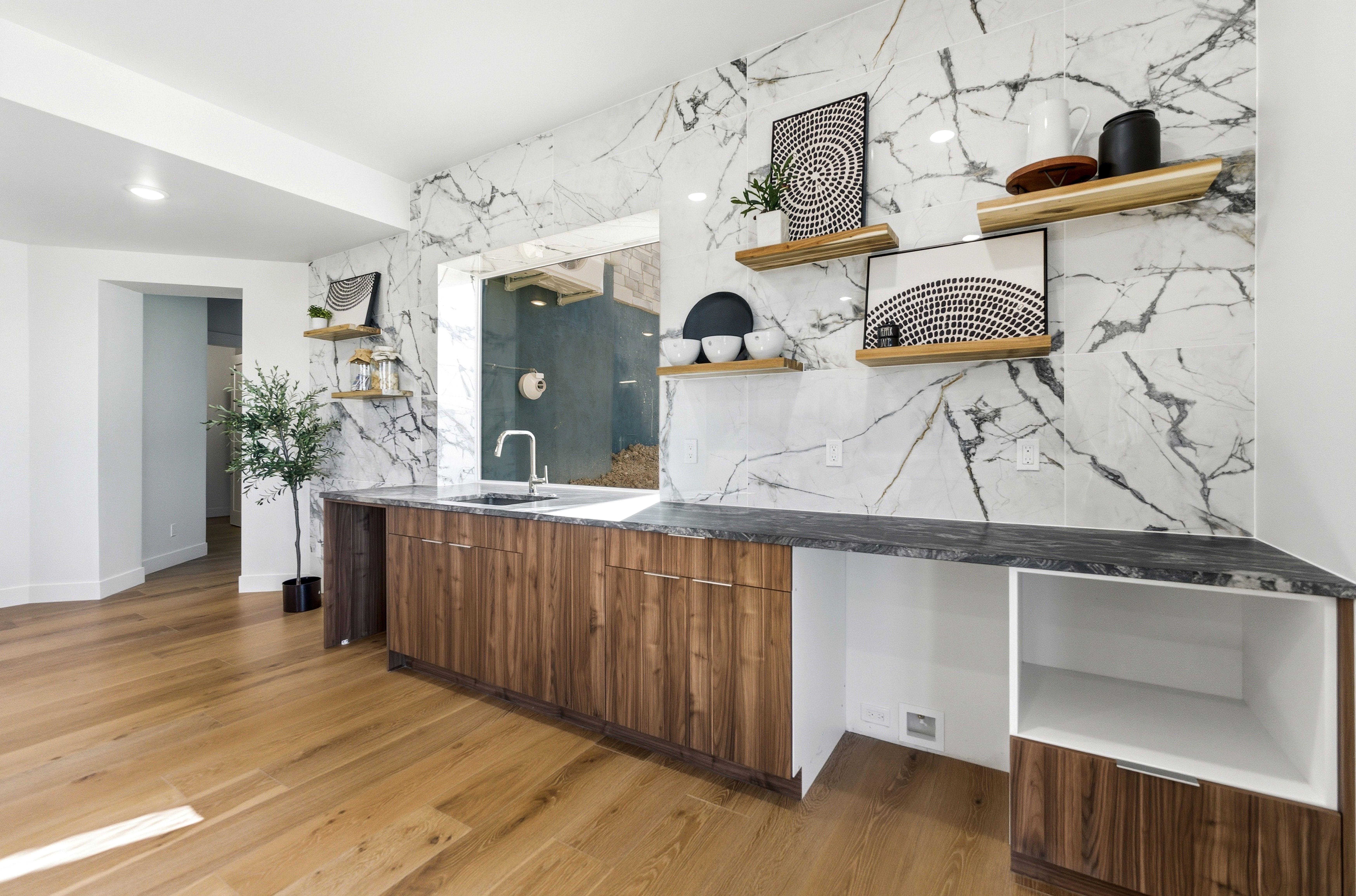 Wet bar area featuring a stone backsplash, integrated sink with a gooseneck faucet, wood-finish cabinetry, and floating wood shelves