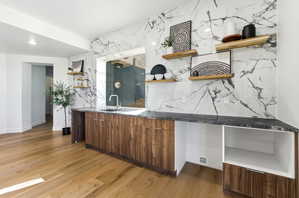Wet bar area featuring a stone backsplash, integrated sink with a gooseneck faucet, wood-finish cabinetry, and floating wood shelves