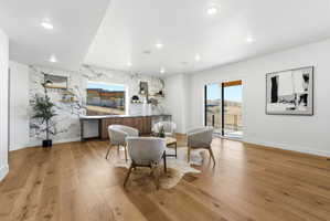 Spacious room featuring wide plank wood flooring, a striking marble-patterned accent wall, recessed lighting, and a built-in wood-finish cabinet with open shelving