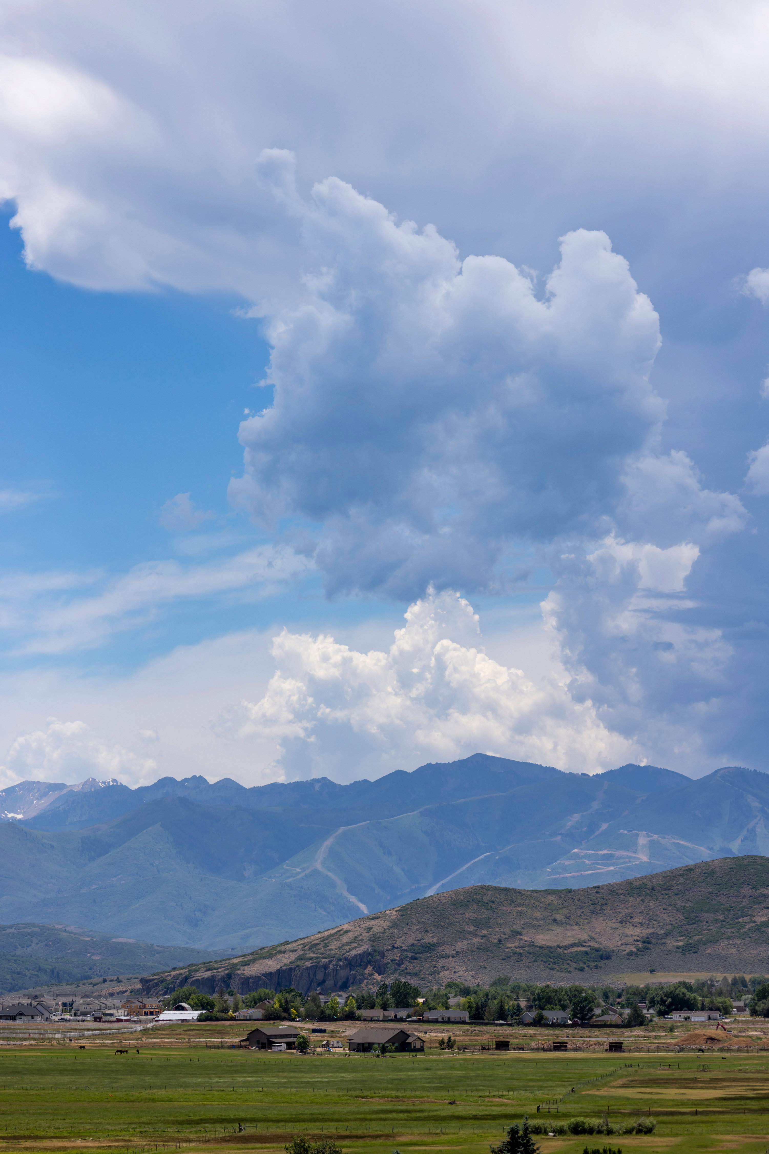 Expansive mountain scenery featuring distant peaks, rolling hills, and a broad green field