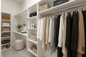 Primary bedroom closet digitally staged -  featuring built-in white shelving, wood-finish flooring, integrated hanging rods, a dedicated vanity area, and recessed lighting