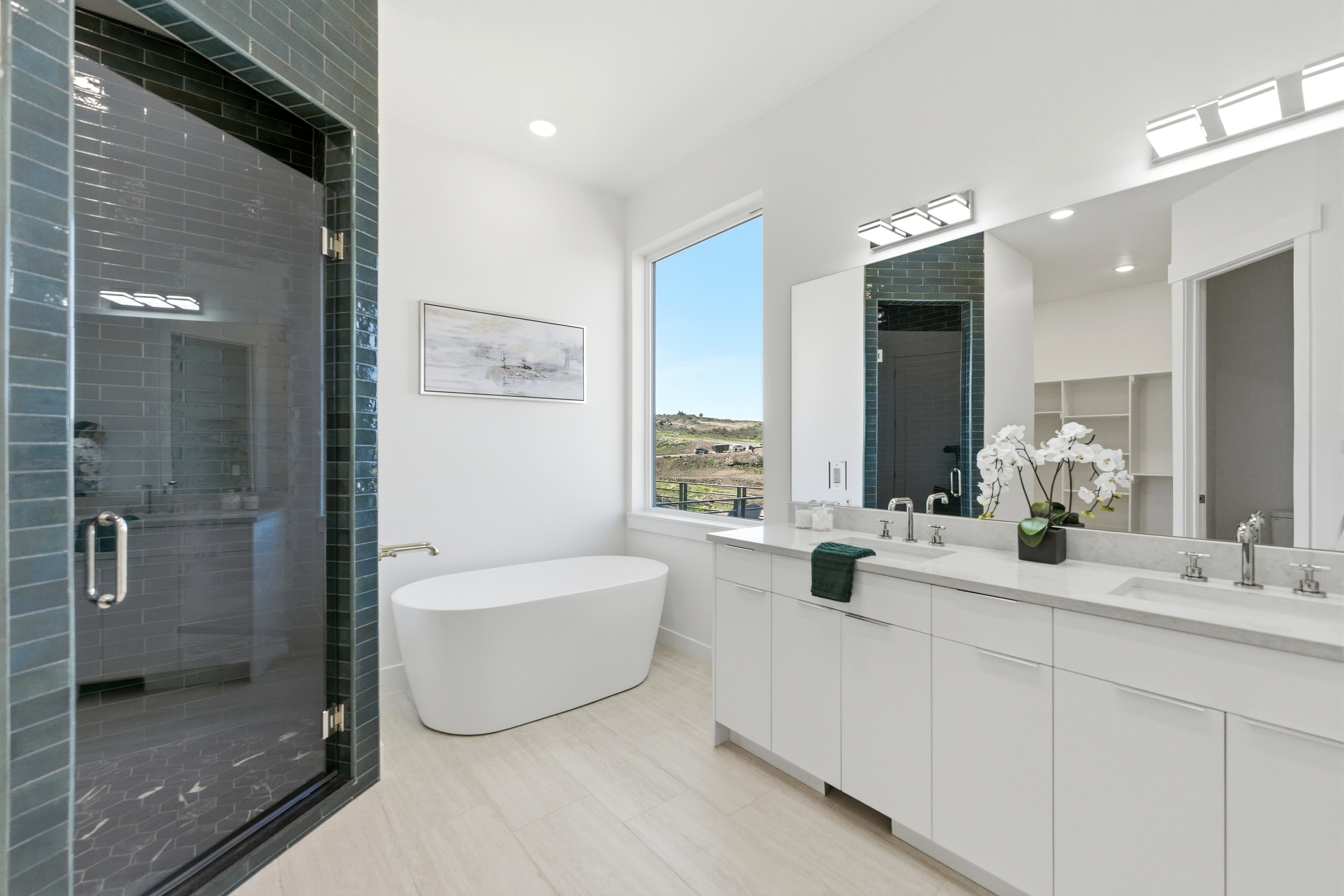 Primary bathroom featuring an elongated freestanding soaking tub, a large walk-in shower with dark subway tile and glass enclosure, a dual vanity with quartz countertop, and light wood-finish flooring