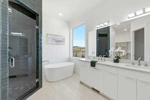 Primary bathroom featuring an elongated freestanding soaking tub, a large walk-in shower with dark subway tile and glass enclosure, a dual vanity with quartz countertop, and light wood-finish flooring