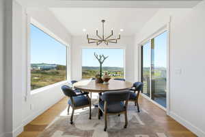 Bright dining area featuring wood-finish flooring, a contemporary chandelier, large picture windows, and a sliding glass door